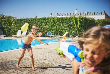 Mädchen und Junge bei einer Wasserschlacht mit Wasserpistole und Wasserbomben am Pool - DIKF00311