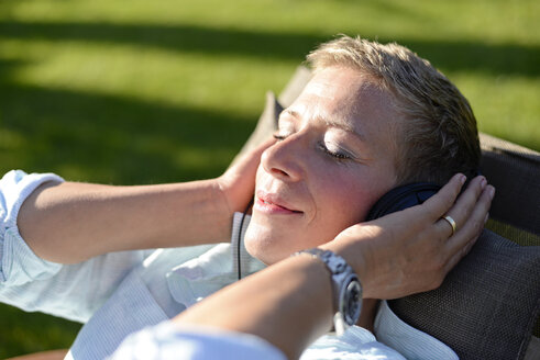 Porträt einer Frau, die mit Kopfhörern im Garten Musik hört - BFRF01929