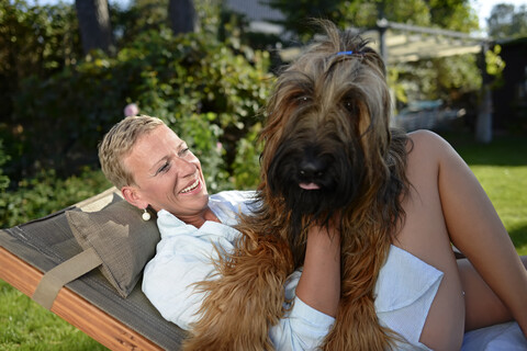 Porträt einer glücklichen Frau, die mit ihrem Hund im Garten kuschelt, lizenzfreies Stockfoto