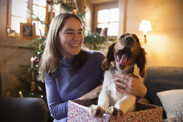 Glückliches Teenager-Mädchen mit gähnendem Hund in Weihnachtsgeschenkbox - HOXF03957