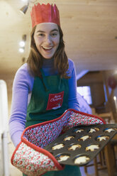 Porträt begeistertes Teenager-Mädchen in Weihnachtsschürze und Papierkrone beim Backen von Muffins - HOXF03961
