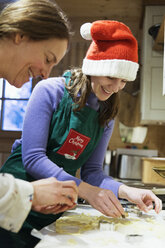 Mutter und Tochter in Weihnachtsschürze und Weihnachtsmannmütze backen in der Küche - HOXF03963