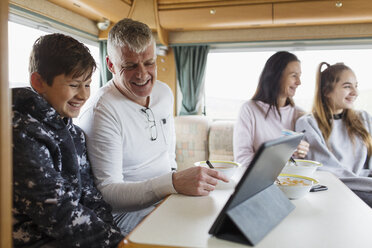 Familie entspannt sich, frühstückt und benutzt ein digitales Tablet im Wohnmobil - HOXF03972