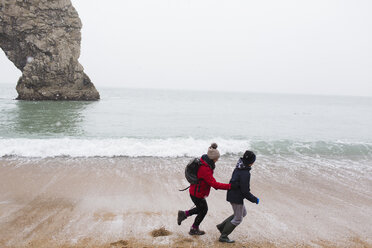 Mutter und Sohn laufen am verschneiten Winterstrand - HOXF03975