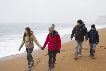 Familie in warmer Kleidung bei einem Spaziergang am verschneiten Winterstrand - HOXF03977