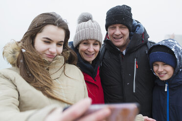 Schnee fällt auf lächelnde Familie, die ein Selfie macht - HOXF03980