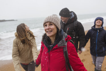 Snow falling over happy family on winter beach - HOXF03984