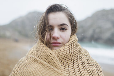 Portrait confident, serious girl with snow in hair wrapped in blanket on winter beach - HOXF03990