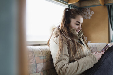 Teenage girl texting with smart phone in motor home - HOXF03993