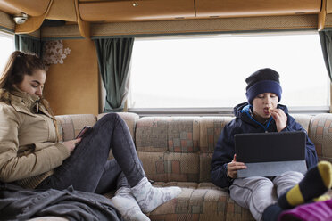 Bruder und Schwester im Teenageralter benutzen Tablet und Smartphone im Wohnmobil - HOXF03997