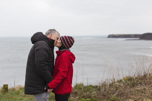 Zärtliches Paar, das sich auf einer Klippe mit Blick auf das Meer küsst - HOXF04000