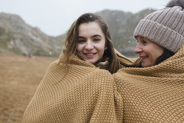 Portrait sorglose Mutter und Tochter in eine Decke eingewickelt am verschneiten Winterstrand - HOXF04003