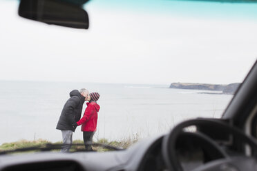 Zärtliches Paar küsst sich außerhalb des Wohnmobils auf einer Klippe mit Blick auf das Meer - HOXF04005