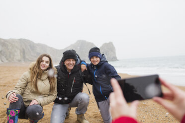 Glückliche Familie posiert für ein Foto am verschneiten Winterstrand - HOXF04008