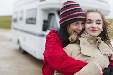 Zärtliche Mutter und Tochter in warmer Kleidung umarmen sich vor dem Wohnmobil - HOXF04009