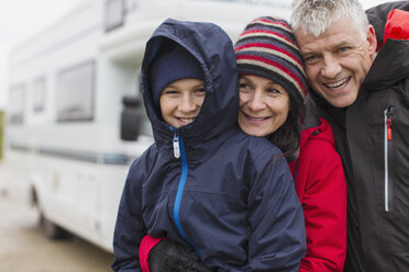 Porträt einer liebevollen Familie in warmer Kleidung, die sich außerhalb des Wohnmobils umarmt - HOXF04015