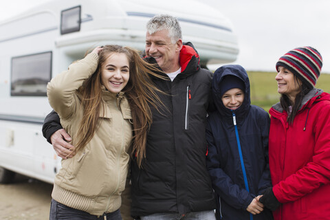 Porträt einer glücklichen Familie in warmer Kleidung vor einem Wohnmobil, lizenzfreies Stockfoto