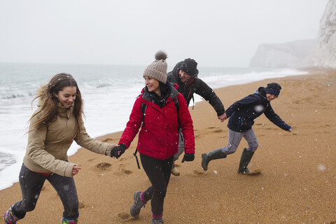 Playful family in warm clothing on snowy winter beach stock photo