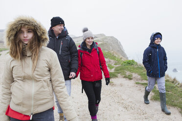 Family in warm clothing walking on snowy winter cliff path - HOXF04038