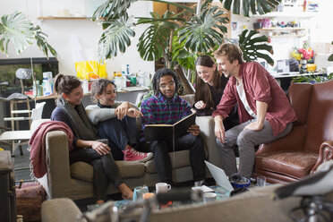 Young adult roommate friends reading book in apartment living room - HOXF04056