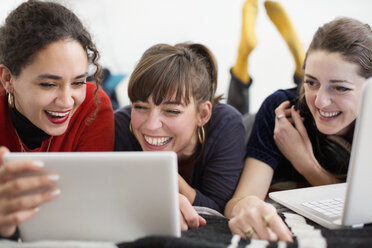 Lachende junge Freundinnen, die sich mit Tablet und Laptop auf dem Bett vergnügen - HOXF04057