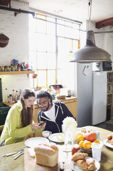 Young couple with smart phone enjoying breakfast in apartment kitchen - HOXF04062
