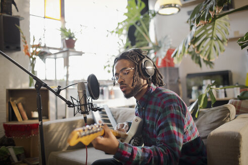 Junger männlicher Musiker, der in einer Wohnung Musik aufnimmt und am Mikrofon Gitarre spielt - HOXF04068