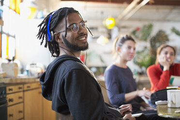 Porträt lächelnder junger Mann mit Kopfhörern am Küchentisch - HOXF04095