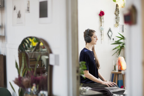 Gelassene junge Frau meditiert mit Kopfhörern in einer Wohnung, lizenzfreies Stockfoto