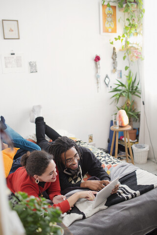 Junges Paar, das sich auf dem Bett mit einem digitalen Tablet entspannt, lizenzfreies Stockfoto