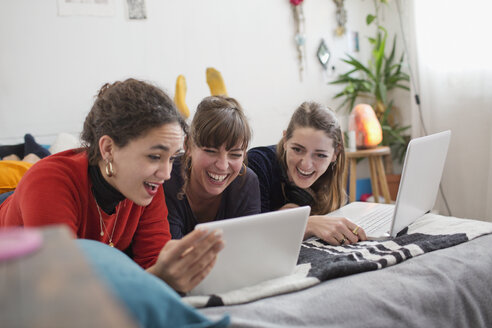 Junge Freundinnen, die auf dem Bett abhängen und ein digitales Tablet und einen Laptop benutzen - HOXF04119