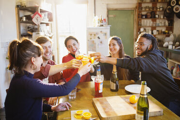 Happy young adult friends toasting cocktails at apartment kitchen table - HOXF04124