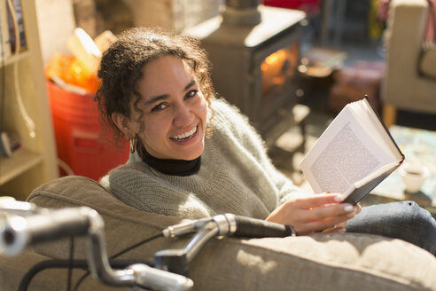 Porträt einer lächelnden, glücklichen jungen Frau, die im Sessel ein Buch liest - HOXF04128