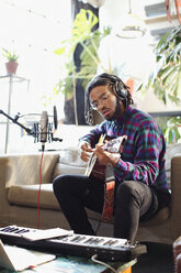 Young man recording music, playing guitar and singing into microphone in apartment - HOXF04138