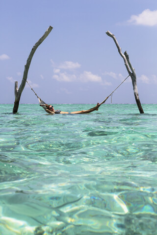 Young woman laying in hammock over tranquil blue ocean, Maldives, Indian Ocean stock photo