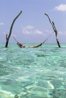 Junge Frau in der Hängematte über dem ruhigen blauen Ozean, Malediven, Indischer Ozean - HOXF04146