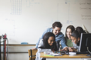 Lächelnde Lehrerin und Schüler bereiten Roboter auf dem Schreibtisch im Klassenzimmer vor - MASF09280