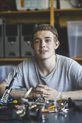 Portrait of confident male teenage student sitting with science project at desk in classroom at high school - MASF09282