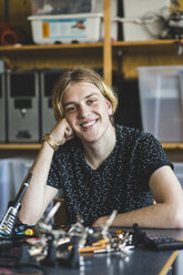 Portrait of smiling young male student sitting with science project at desk in classroom at high school - MASF09283