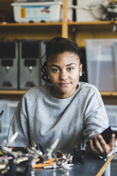 Portrait of confident female teenage student sitting with science project at desk in classroom at high school - MASF09285
