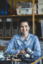 Portrait of confident mature female teacher sitting with science project at desk in classroom at high school - MASF09287