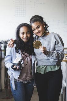 Porträt einer erfolgreichen Schülerin, die einen Roboter und eine Goldmedaille in der Hand hält, während sie im Klassenzimmer einer High School steht - MASF09289