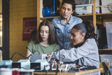 Female teacher looking at high school teenage students preparing robot on desk in classroom - MASF09293