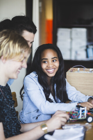 Lächelnde Gymnasiasten bereiten Spielzeugautos am Schreibtisch vor, während der Lehrer im Klassenzimmer steht, lizenzfreies Stockfoto