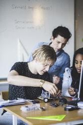 Mature female teacher looking at students preparing toy car on desk in classroom - MASF09301