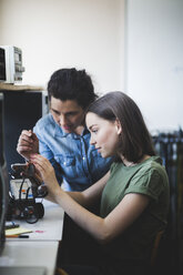 Female teacher assisting teenage student preparing robot on desk in classroom at high school - MASF09302