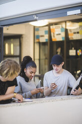 Multiethnische Schüler nutzen Smartphones, während sie an einer Stützmauer in der High School stehen - MASF09308