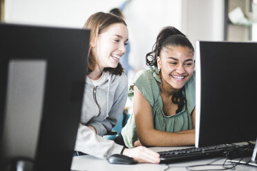 Fröhliche multiethnische Teenager-Mädchen, die am Schreibtisch im Computerlabor einer High School diskutieren - MASF09316
