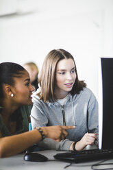 Multi-ethnic teenage girls discussing over computer monitor at desk in classroom - MASF09318