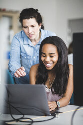 Selbstbewusste Lehrerin, die einer lächelnden Schülerin hilft, einen Laptop am Schreibtisch im Klassenzimmer zu benutzen - MASF09319